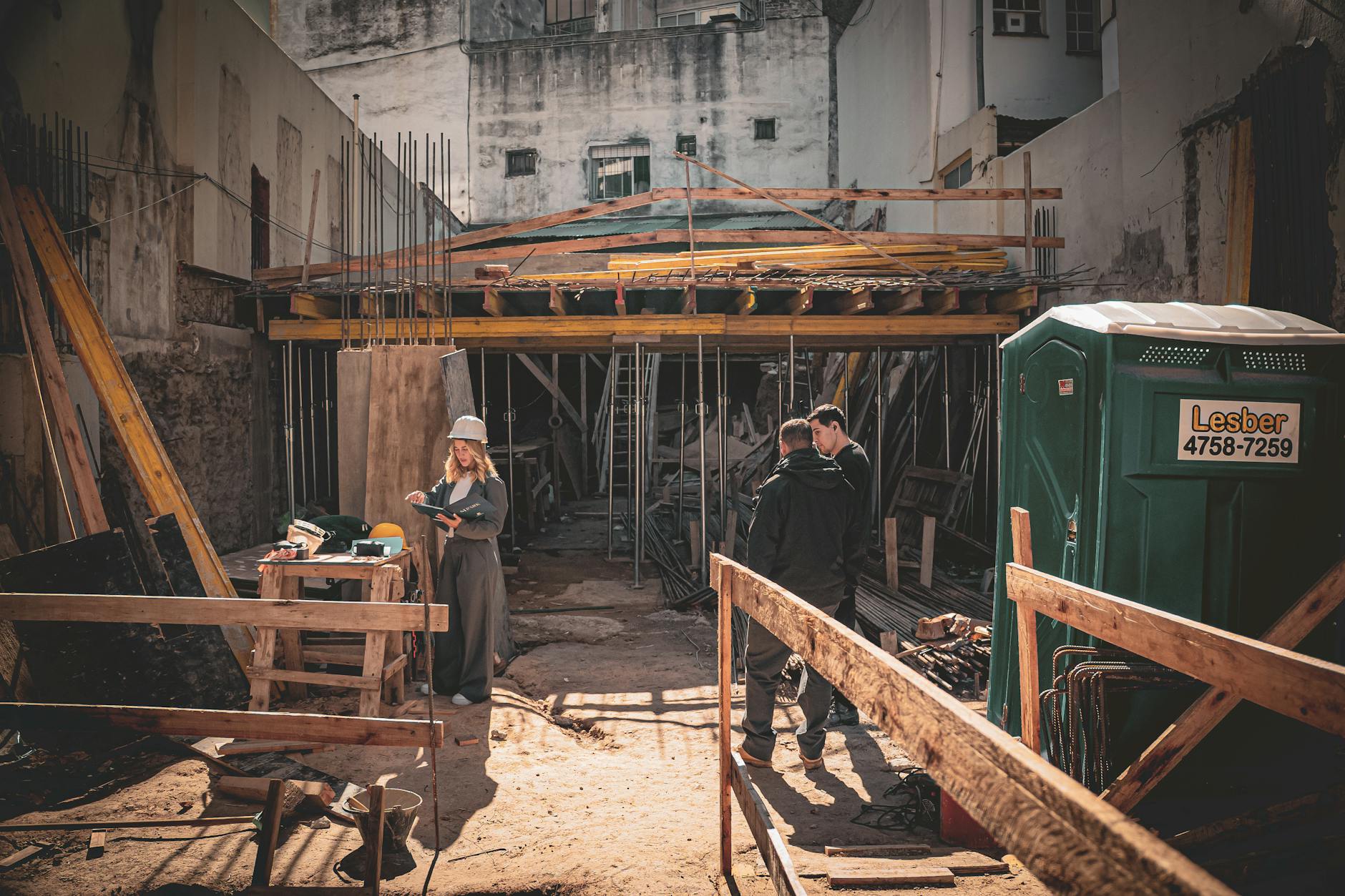 Canteiro de obras com operários e arquiteto analisando plantas sob a luz do dia.