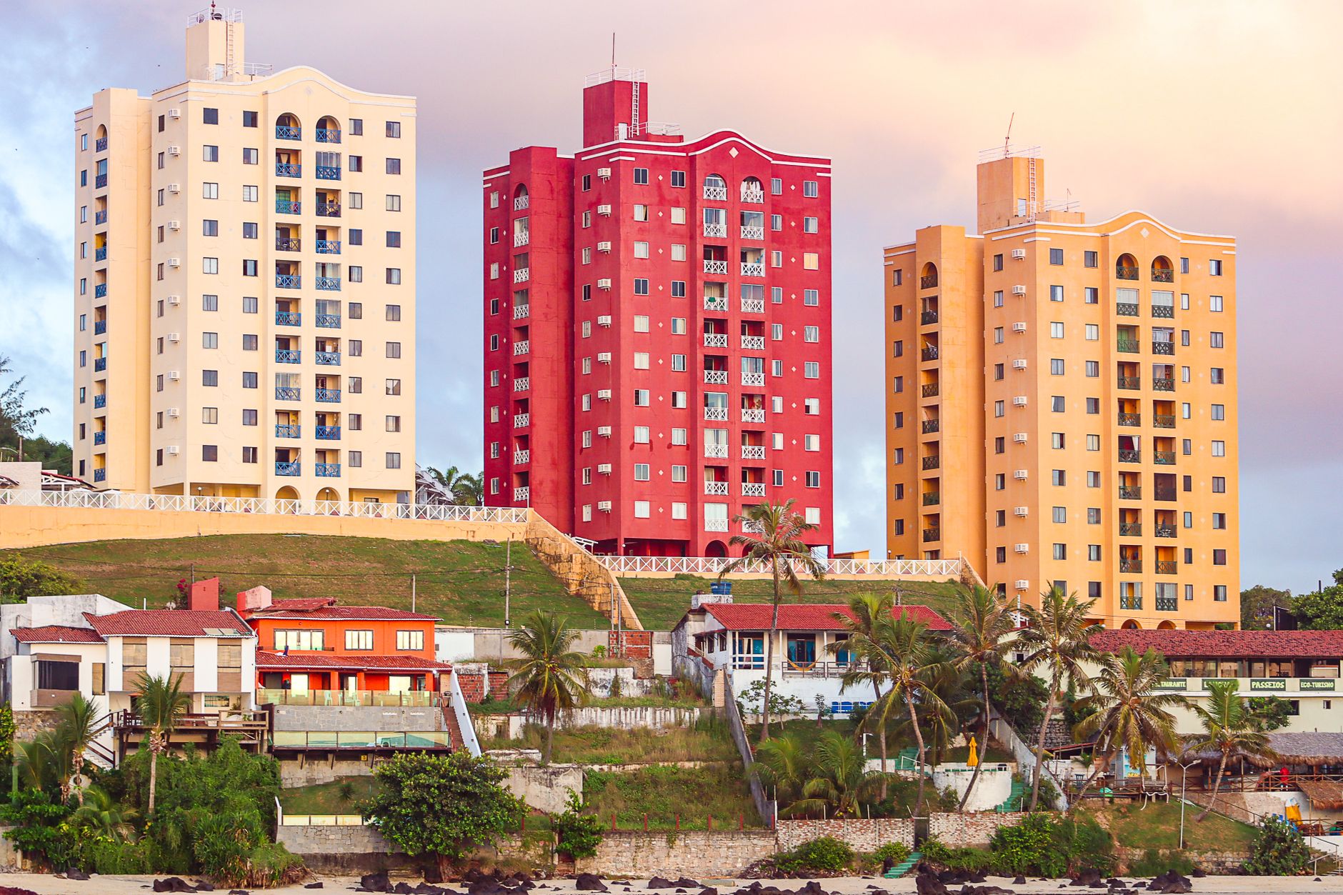 Prédios residenciais compactos em área urbana com fachadas que evidenciam unidades pequenas, em ambiente com luz natural e cores quentes.
