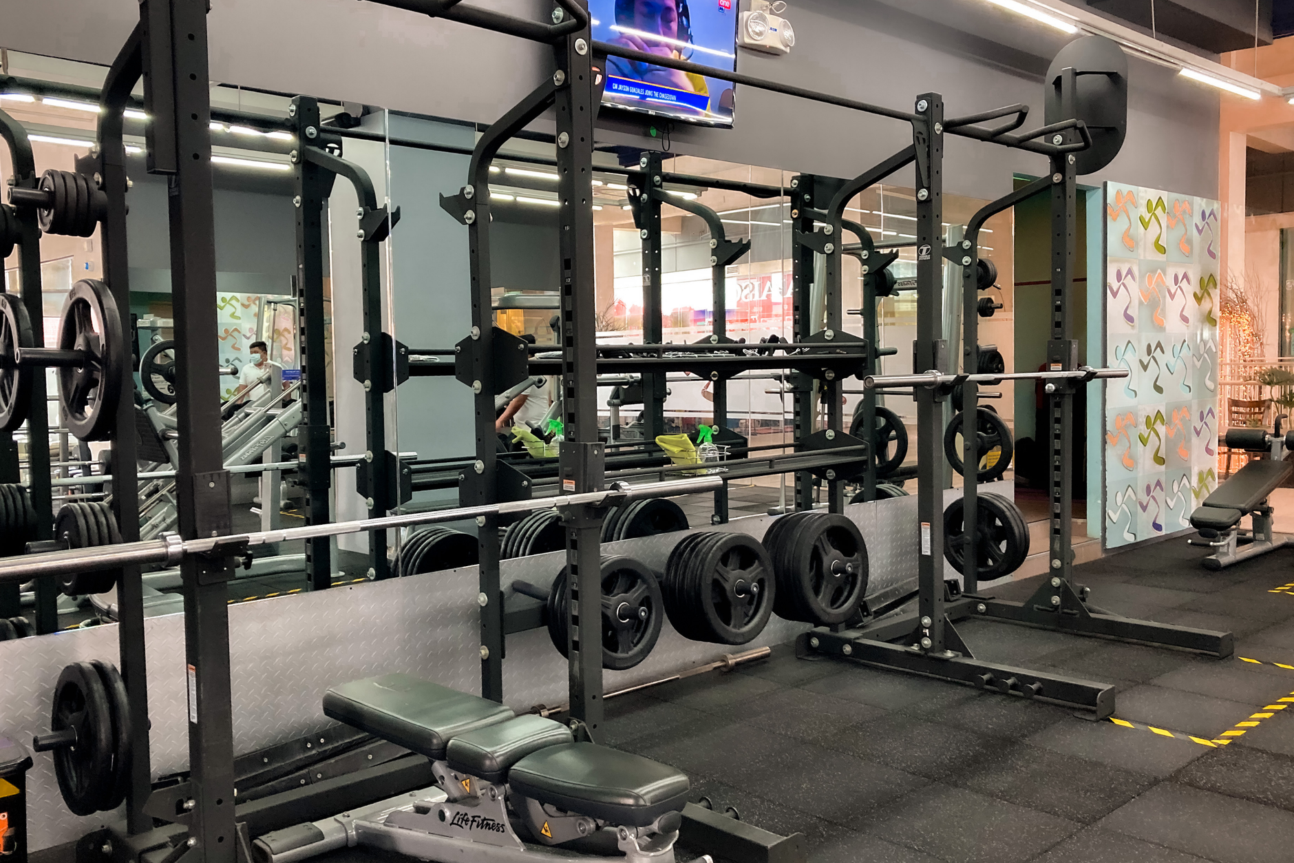 Interior de academia instalada em espaço que remete a antiga agência bancária, com equipamentos de ginástica e elementos arquitetônicos do banco.